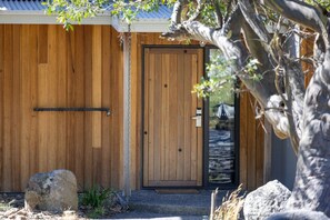 A wooden building with a door, a metal gate, and a large tree in front. - Rose Creek Chalet: Cosy 2BR w/ Resort Facilities, Crackenback Resort NSW (Crackenback)