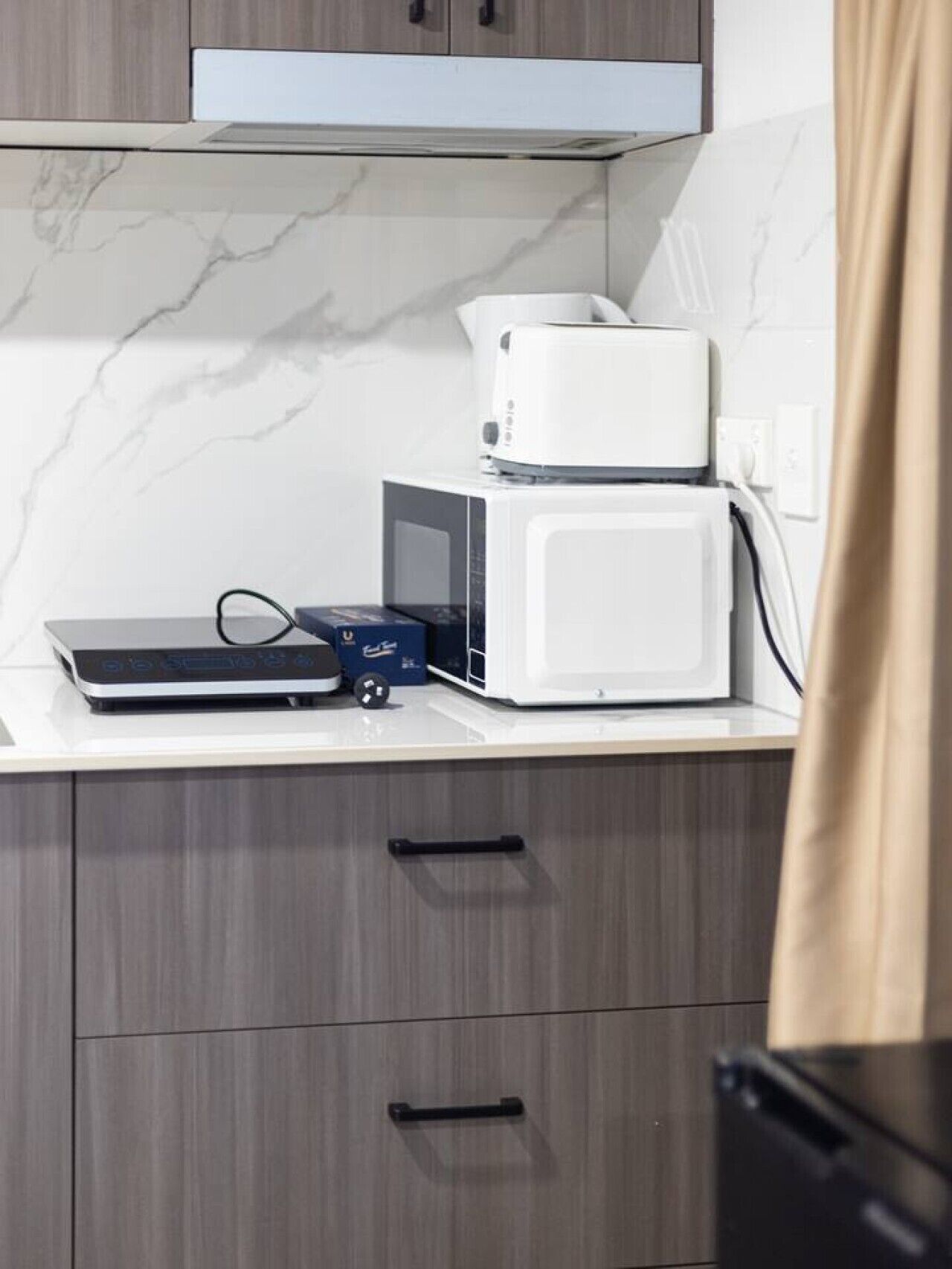 A kitchen with a microwave, a toaster, and a small appliance on the counter. There are cabinets below and a curtain partially visible.