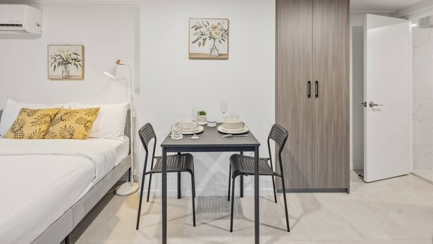 A modern bedroom with a bed, bedside table, and a dining area with a table and chairs. - Great Value|Renovated Studio|Prime Location|Aircon (Nathan)