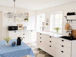A kitchen with white cabinetry, a checkered tablecloth, a black kettle, and a chandelier.