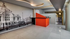 A modern interior with a mural of a historical building, a red reception desk, and a staircase.