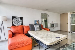 Ein modernes Wohnzimmer mit einer Couch, einem Schlafsofa, einem Wand-Fernseher und einem großen Fenster.