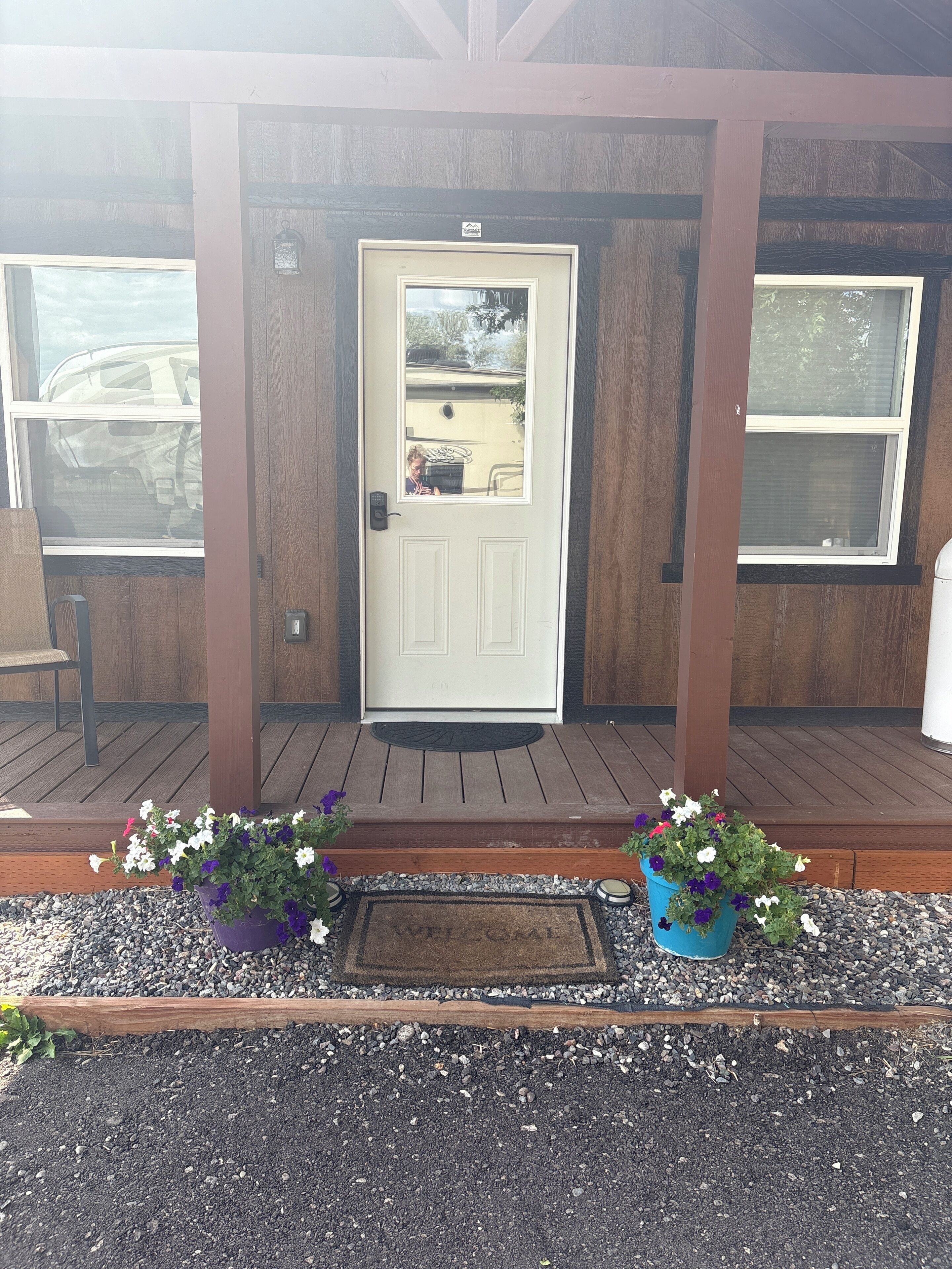 A wooden house with a white door, a porch with a bench, and two flower pots.