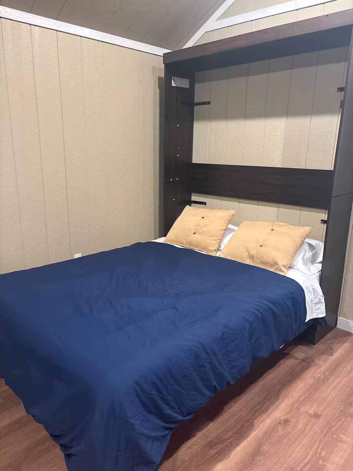 Un dormitorio con cama, suelo de madera y cabecero con espejo.