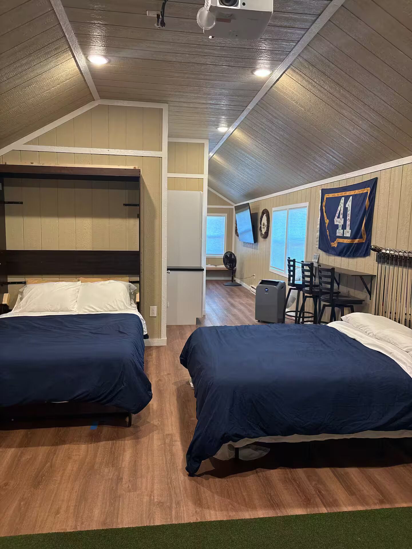 A room with two beds, a desk, a chair, a radiator, and a flag on the wall.