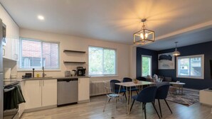 A modern kitchen with a dining area, large windows, and a ceiling light fixture.