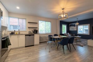 A modern kitchen with a dining area, large windows, and a ceiling light fixture.
