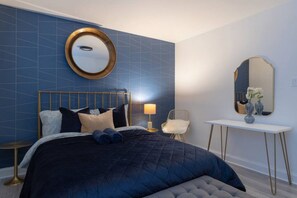 A bedroom with a large bed, a bedside table with a lamp, a chair, and a mirror.