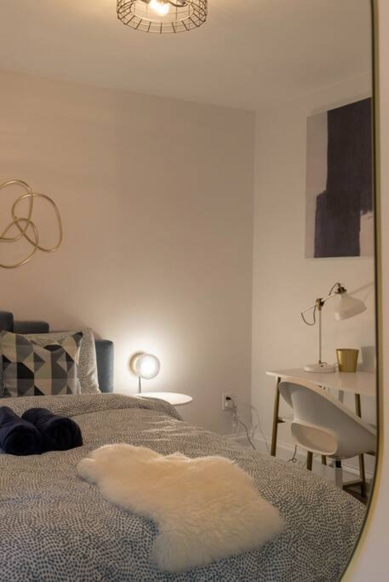 A bedroom with a bed, a desk, a chair, a lamp, and a mirror.