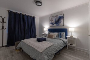 A modern bedroom with a bed, two bedside tables, a headboard, a painting, and a coat rack.