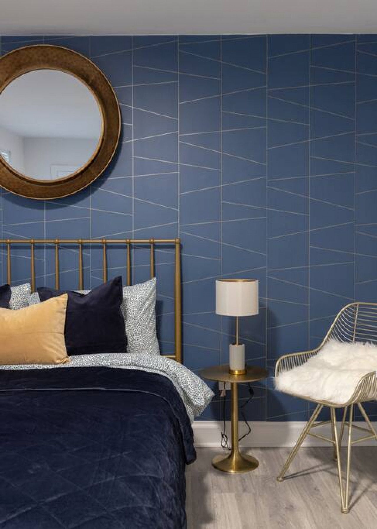 A bedroom with a bed, a round mirror, a bedside table with a lamp, and a chair.