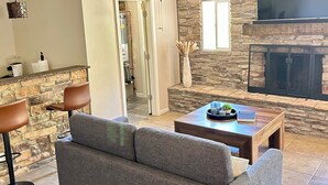 A living room with a stone fireplace, a grey sofa, a coffee table, and a ceiling fan. - Scottsdale Paradise w/ Fire Pit & BBQ, Heated Pool & Spa, Mini Golf & Cornhole (Scottsdale)
