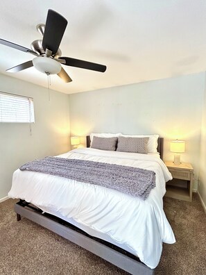 Ein Schlafzimmer mit einem Bett, zwei Nachttischlampen, einem Deckenventilator und einem Fenster mit Jalousien.