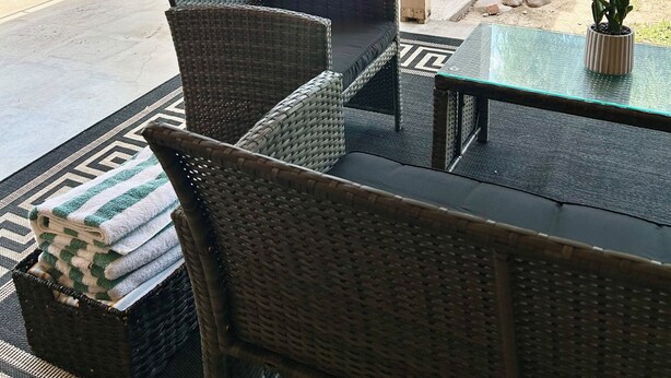 An outdoor patio with wicker furniture, a glass table, and a view of a swimming pool. - Scottsdale Paradise w/ Fire Pit & BBQ, Heated Pool & Spa, Mini Golf & Cornhole (Scottsdale)