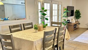 A dining area with a table set for six, surrounded by chairs, a hanging light fixture, and a television mounted on the wall. - Scottsdale Paradise w/ Fire Pit & BBQ, Heated Pool & Spa, Mini Golf & Cornhole (Scottsdale)