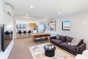 A modern living room with a sofa, coffee table, and a dining area with chairs and a table. - Inner City for Large Groups - Garage Parking (Christchurch)
