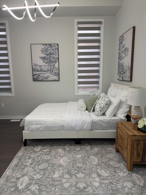 Un dormitorio con cama, mesita de noche, lámpara y dos cuadros en la pared.