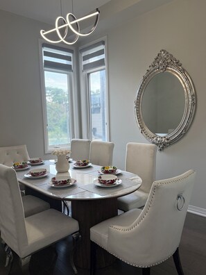 A dining area with a round table, white chairs, and a decorative mirror. - Luxury Waterfront Retreat | Walk to Beach | Sleeps 18 (Clarington)