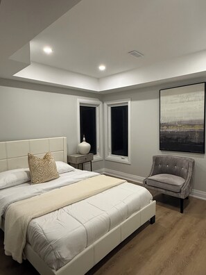 A bedroom with a large bed, a nightstand, a chair, and a window. - Luxury Waterfront Retreat | Walk to Beach | Sleeps 18 (Clarington)