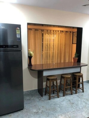A kitchen with a black refrigerator, a wooden counter, and three wooden stools.