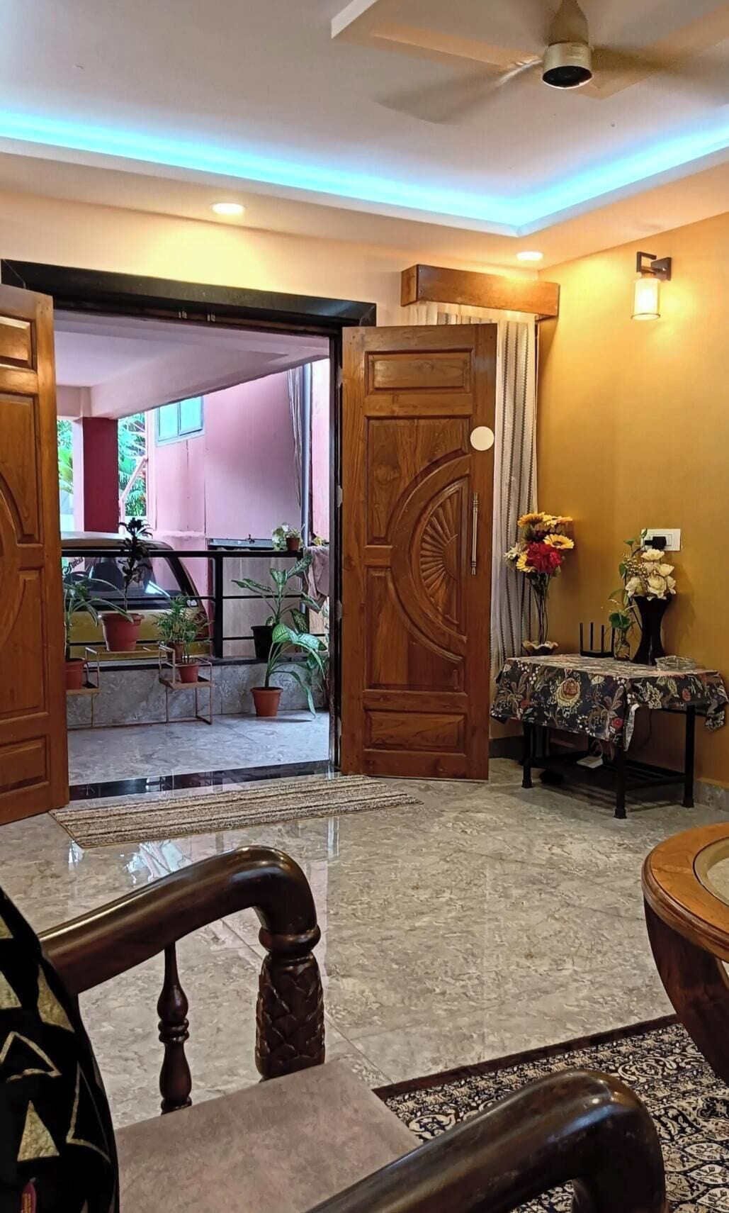 A hotel lobby with a wooden door, a reception desk, a chair, and a table with a vase of flowers.
