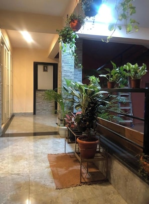 A hallway with a marble floor, potted plants, and a staircase with a railing.