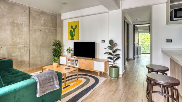 Uma sala de estar moderna com um sofá verde, uma TV de tela plana, uma mesa de centro de madeira e um tapete colorido.