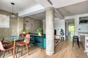 A modern interior with a dining area featuring a glass table, red chairs, and a green sofa. A large pillar and a hanging light fixture are visible. - Roma Elegance · Unique Apartment (Ciudad de México)