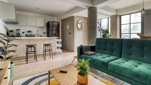 Um espaço de estar moderno com um sofá verde, uma área de cozinha e uma janela grande.