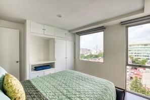 Un dormitorio con cama, armario, ventana y vista a la ciudad.