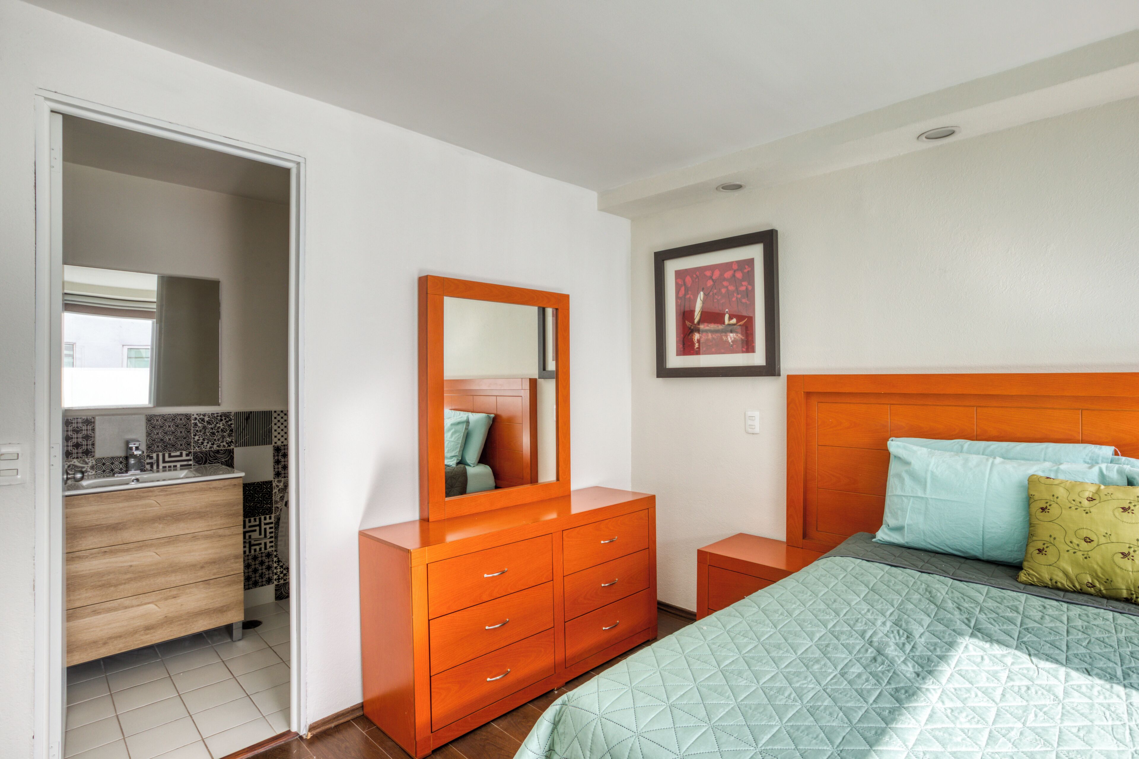 A bedroom with a bed, a dresser, a mirror, and a framed picture on the wall.