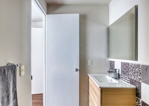 A bathroom with a white door, a towel hanging on a hook, a sink with a mirror above it, and patterned tiles on the wall. - Juárez Elegance · A Pasos del Ángel (Ciudad de México)
