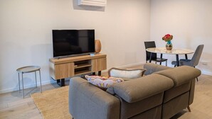 A modern living room with a flat-screen TV, sofa, coffee table, and dining area. - `Heart of Canberra` ~ Inner City 1br apartment (Reid)