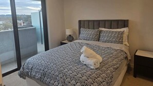 A hotel room with a large bed, a nightstand with a lamp, and a view through a glass door. - Classy 2b2b apartment / Northbourne Ave (Dickson)