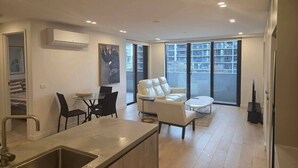 A modern kitchen with a built-in sink and dining area, a white sofa, and a large window with a view. - Classy 2b2b apartment / Northbourne Ave (Dickson)