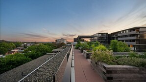 A rooftop terrace with a gravel path, wooden planters with greenery, and modern buildings in the background. - Classy 2b2b apartment / Northbourne Ave (Dickson)