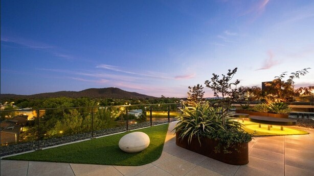 A rooftop terrace with a view of a cityscape and hills, featuring a seating area with planters and a spherical bench. - Classy 2b2b apartment / Northbourne Ave (Dickson)