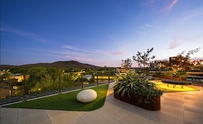 Terraza en la azotea con vistas a un paisaje urbano y colinas, que cuenta con una zona de estar, macetas y un banco esférico.