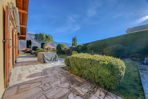A stone-paved outdoor area with a table and chairs, surrounded by well-maintained hedges and a mountain backdrop. - Beautiful Family Home with a Pool, Nestled Between the Lake and the Mountains (Lathuile)