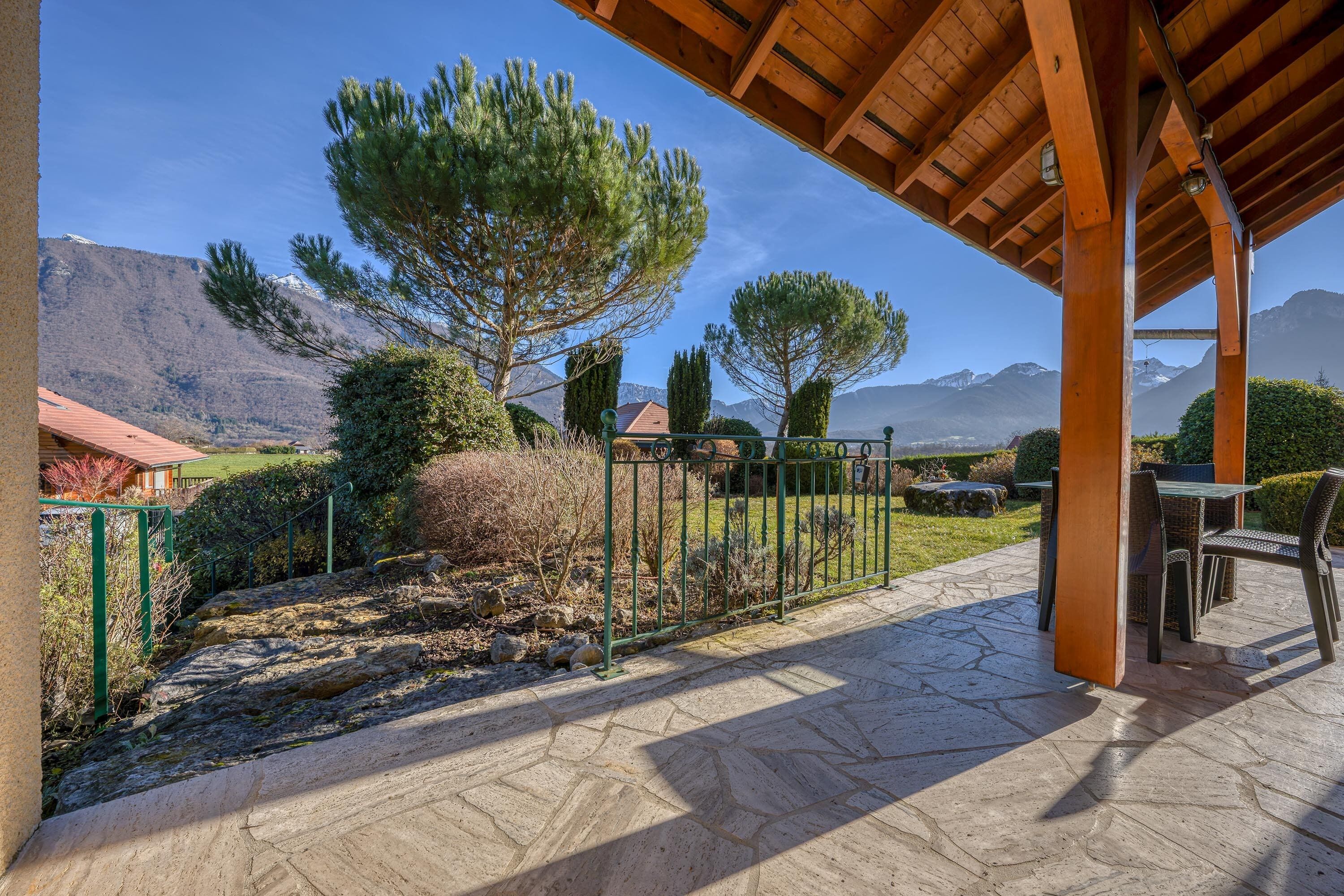 A covered outdoor area with a stone patio, a table and chairs, and a view of mountains in the background.