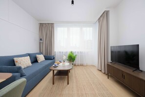 A modern living room with a blue sofa, a coffee table, a TV, and a plant. - Stylish Apartment with Loggia | 2 Bedrooms | Workspace (Warszawa)