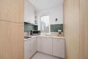 A compact kitchen with white cabinetry, a microwave, a kettle, and a sink. - Stylish Apartment with Loggia | 2 Bedrooms | Workspace (Warszawa)