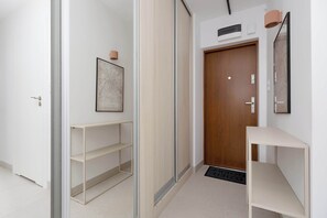 A hallway with a wooden door, a white wall with a framed map, and a white shelf unit. - Stylish Apartment with Loggia | 2 Bedrooms | Workspace (Warszawa)