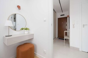 Une salle de bain moderne avec un miroir rond, un meuble-lavabo blanc, une petite plante et un tabouret marron.