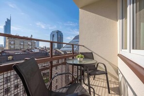 A balcony with a table and chairs, a potted plant, and a view of city buildings. - Stylish Apartment with Loggia | 2 Bedrooms | Workspace (Warszawa)