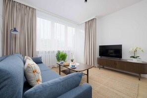 A modern living room with a sofa, a coffee table, a TV, and a potted plant. - Stylish Apartment with Loggia | 2 Bedrooms | Workspace (Warszawa)