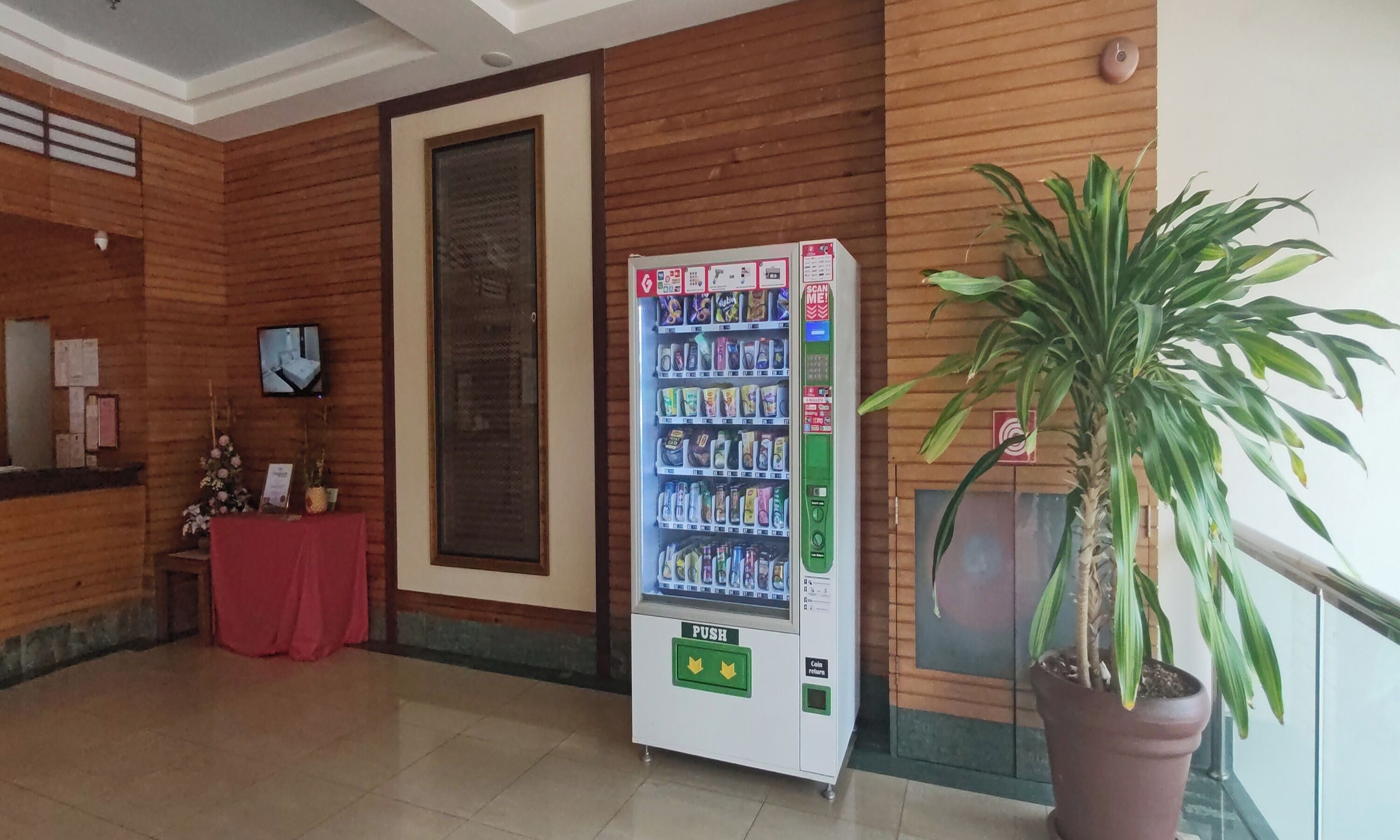 A reception area with a vending machine, a potted plant, and a wooden wall.