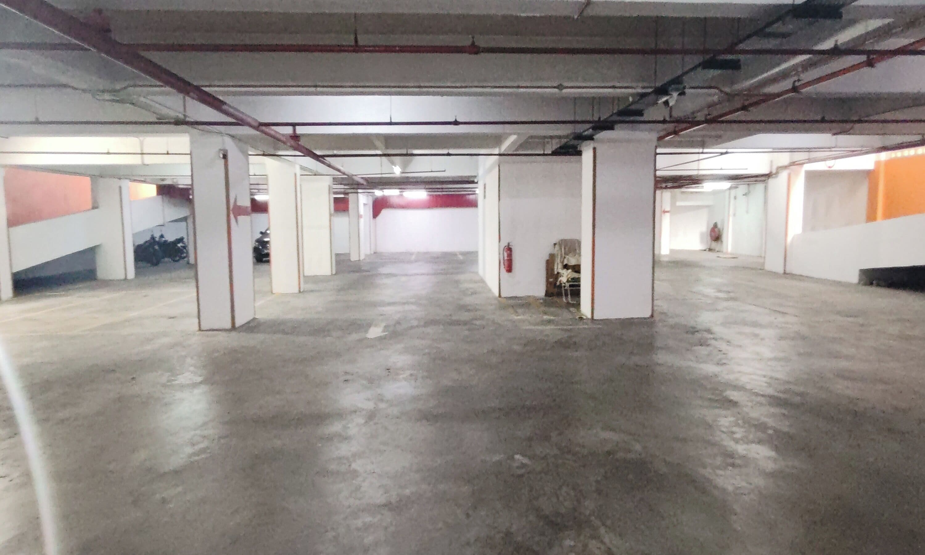 Amplio estacionamiento interior con pisos de concreto y pilares blancos.