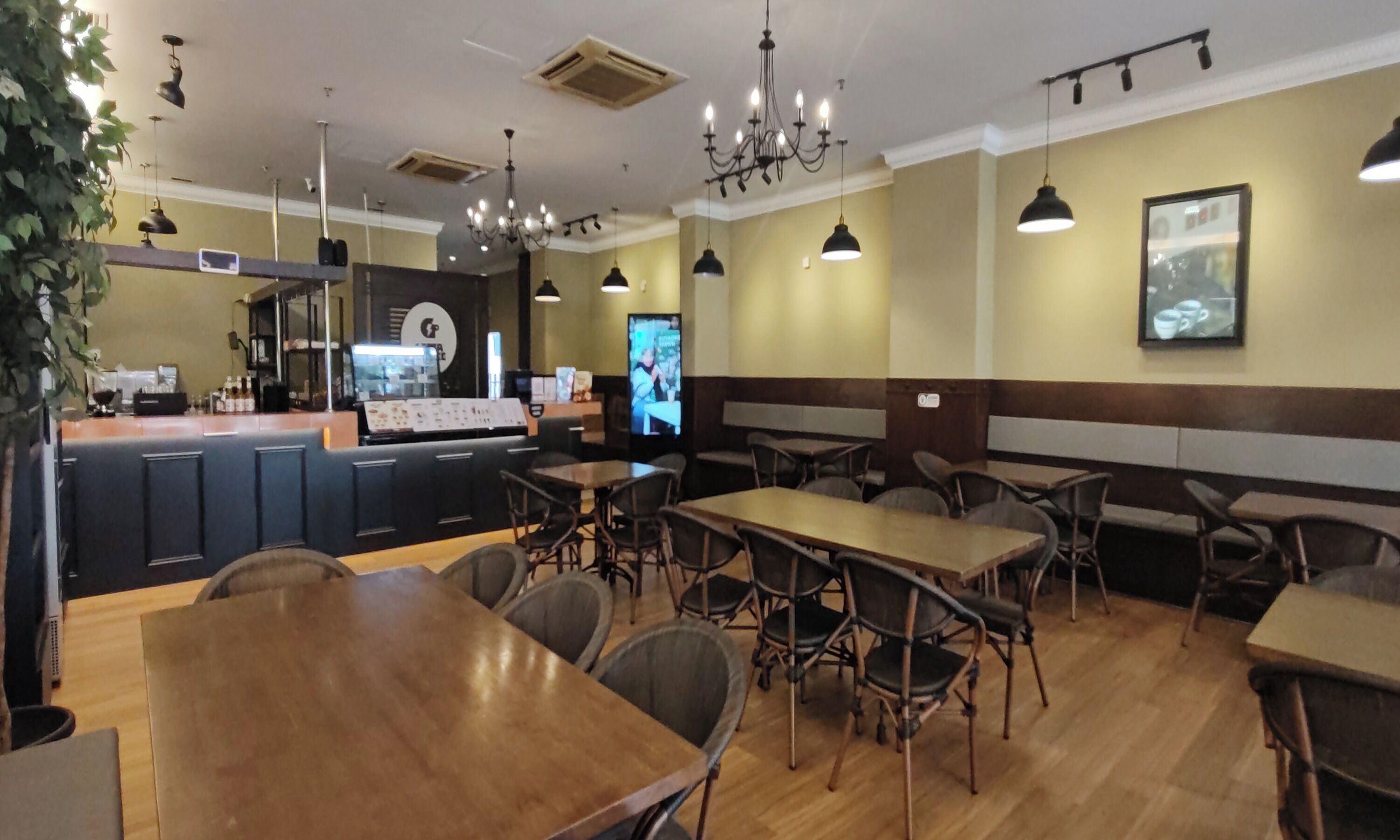 Interior de restaurante con mesas y sillas de madera, una barra con menú y una pantalla de televisión.