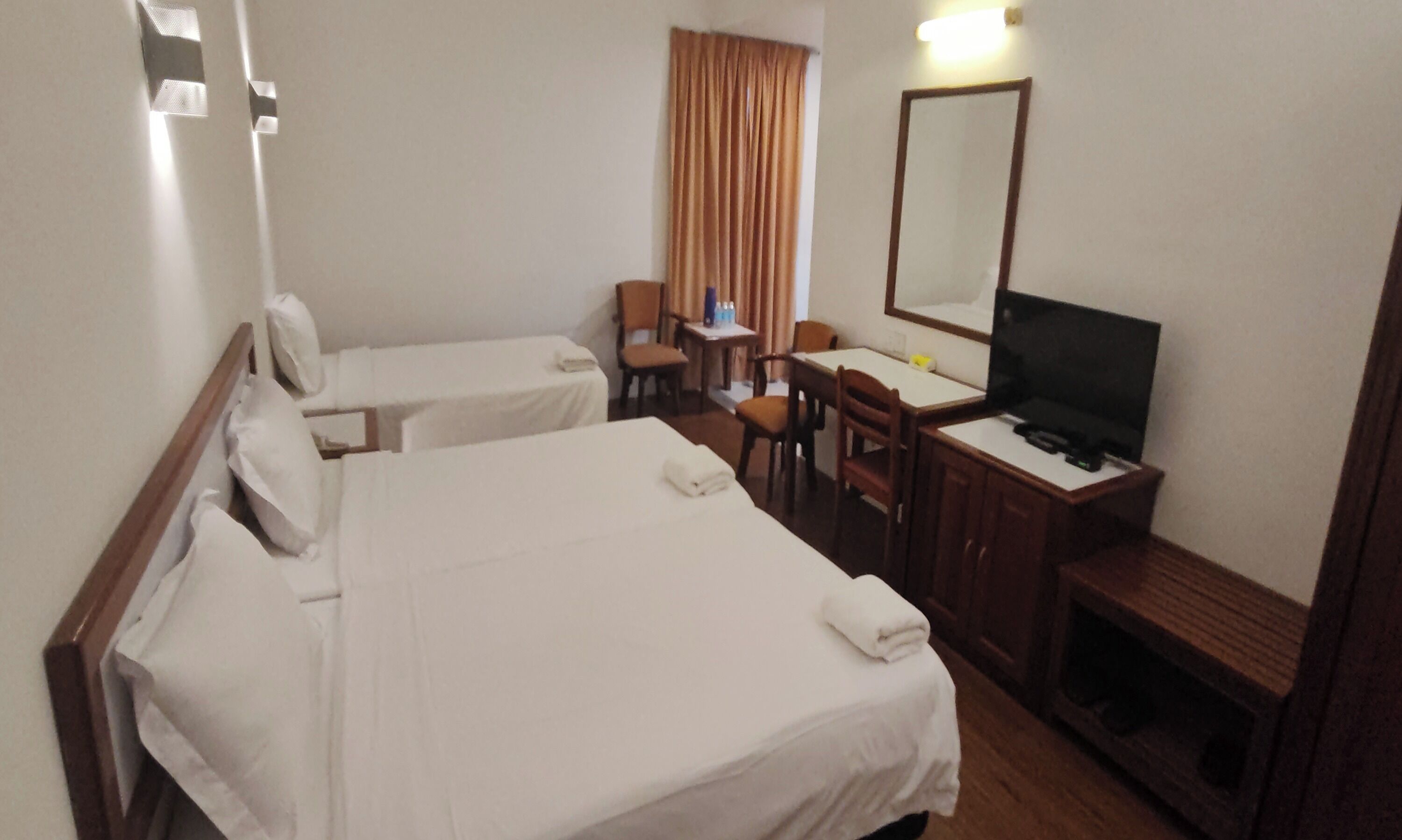 A hotel room with two single beds, a desk with a chair, a television, and a mirror.